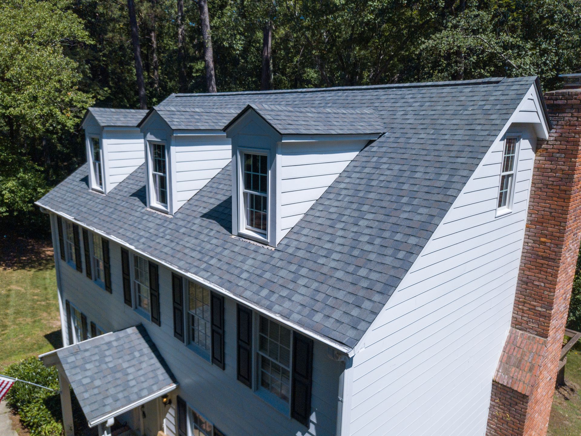 Two-story house with a gray shingle roof, three dormers, and a brick chimney.