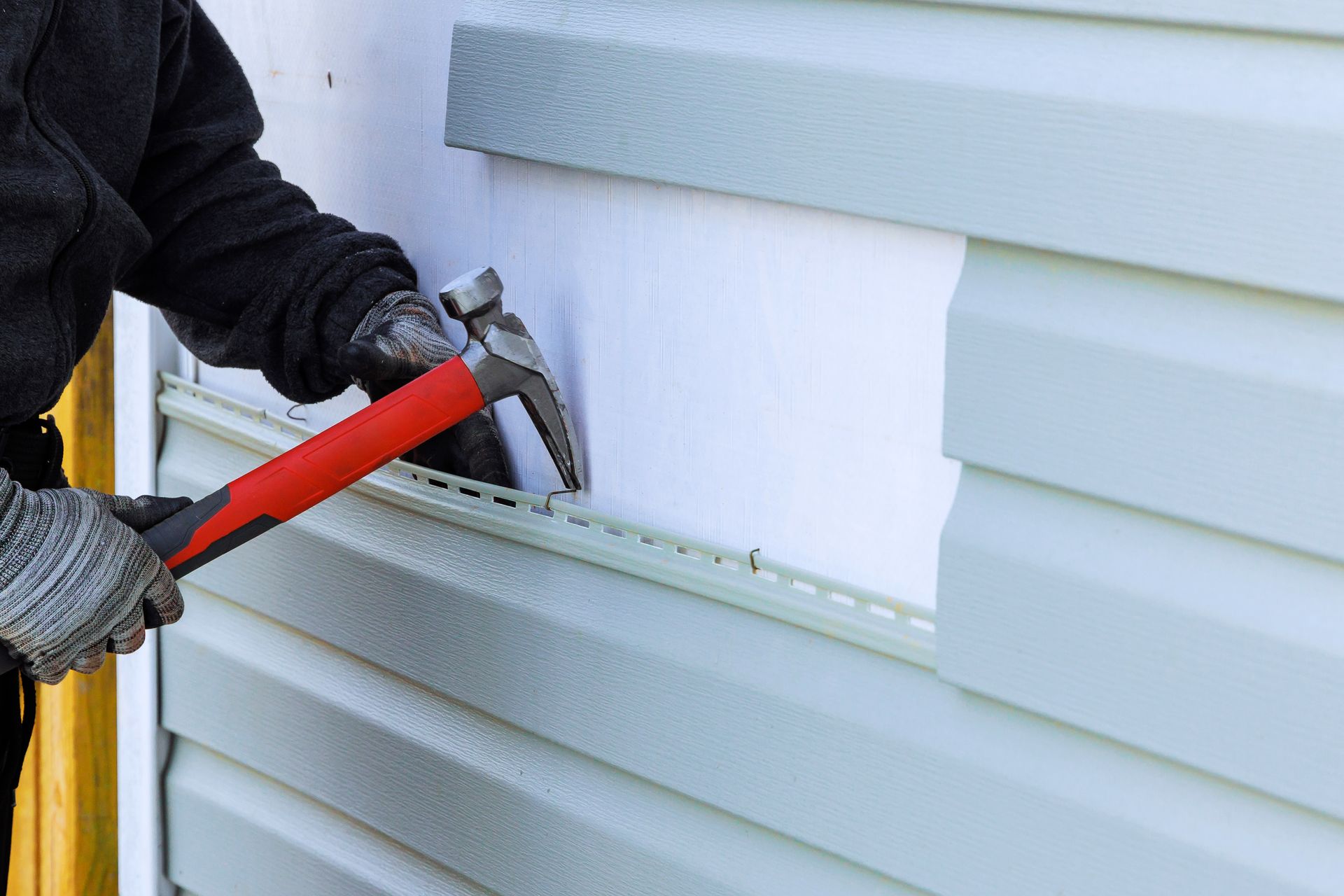 Person using a hammer to remove siding from a house.
