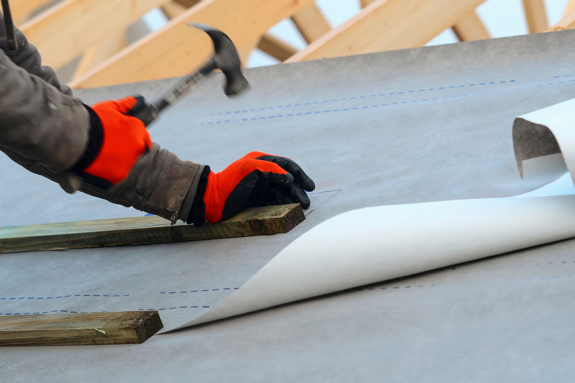 Person hammering wood on a roof, wearing orange gloves.