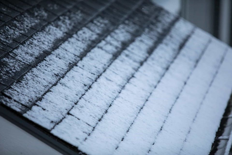 Snow-covered roof with a linear pattern of dark shingles and icy white frost.