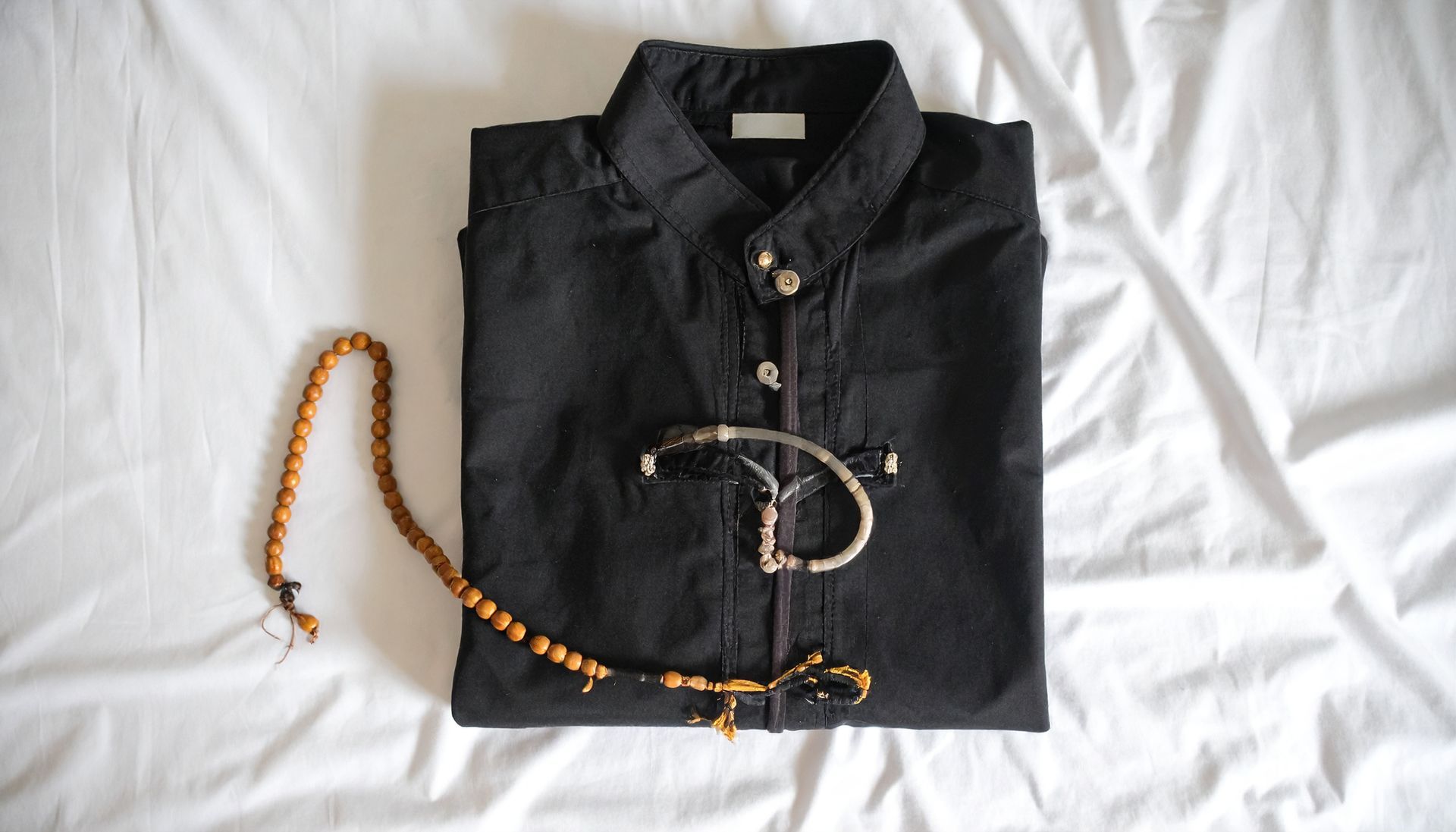 Black shirt folded on white fabric, with a beaded strand and metal bracelet.
