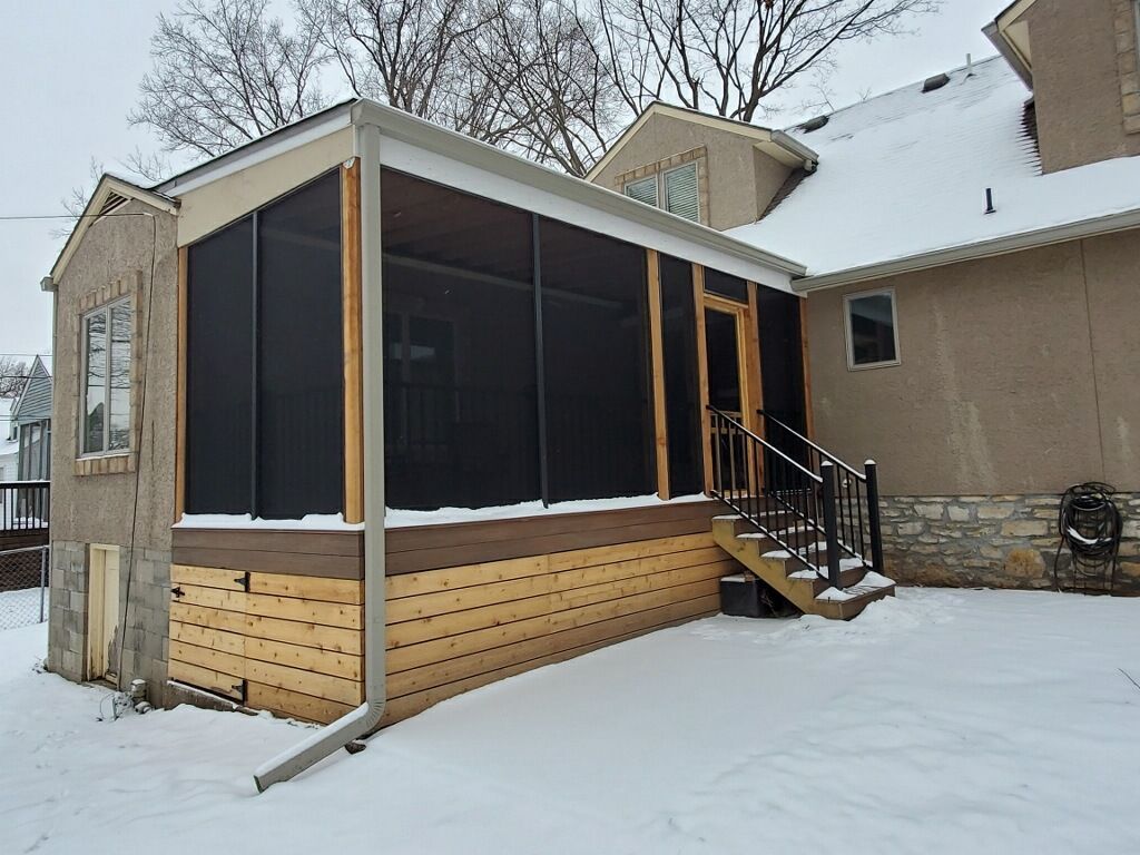 A screened in porch with stairs in the snow next to a house.