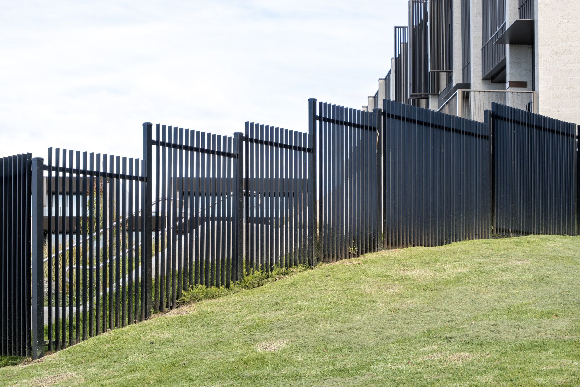 Tall black metal fence running along a grassy slope beside modern apartment buildings