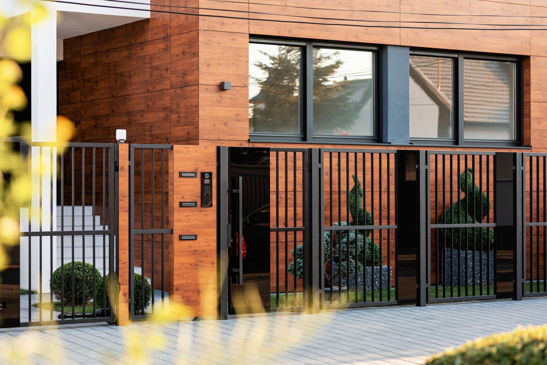 Modern house exterior with wood siding, black metal fence and gate, and large windows