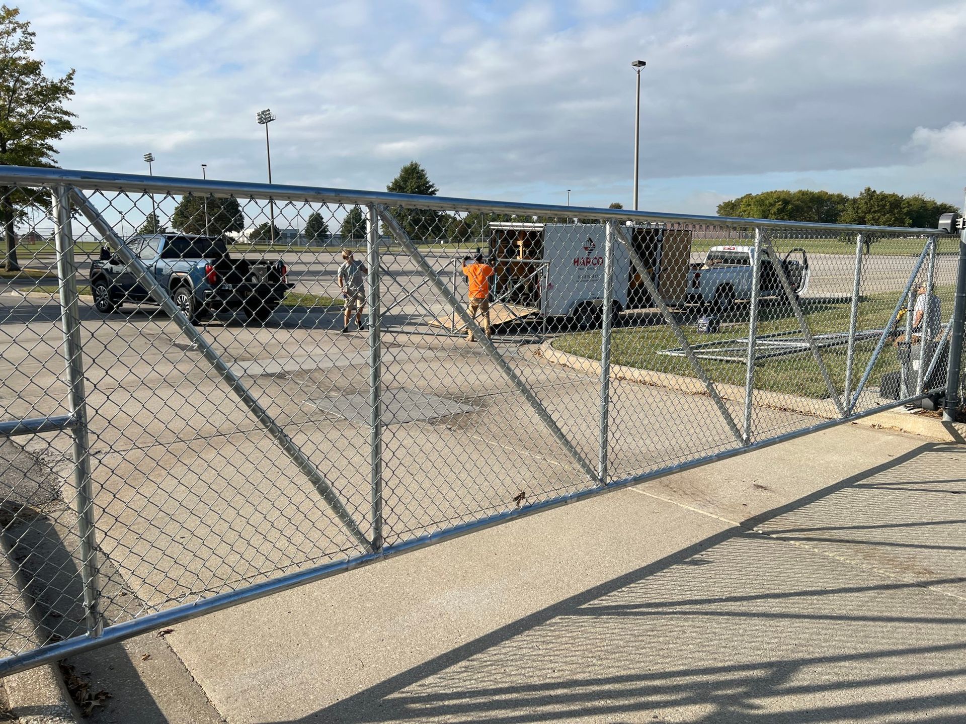 A chain link fence is being installed in a parking lot.