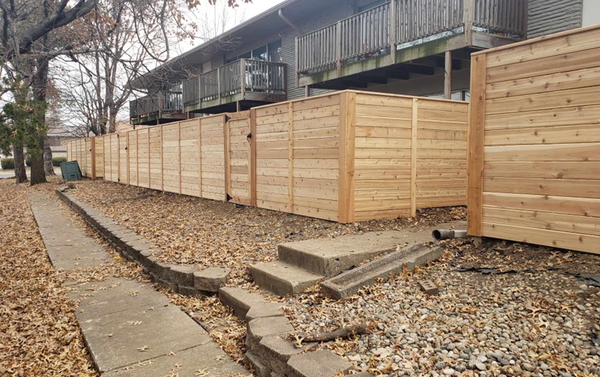 A wooden fence along a sidewalk next to a building.