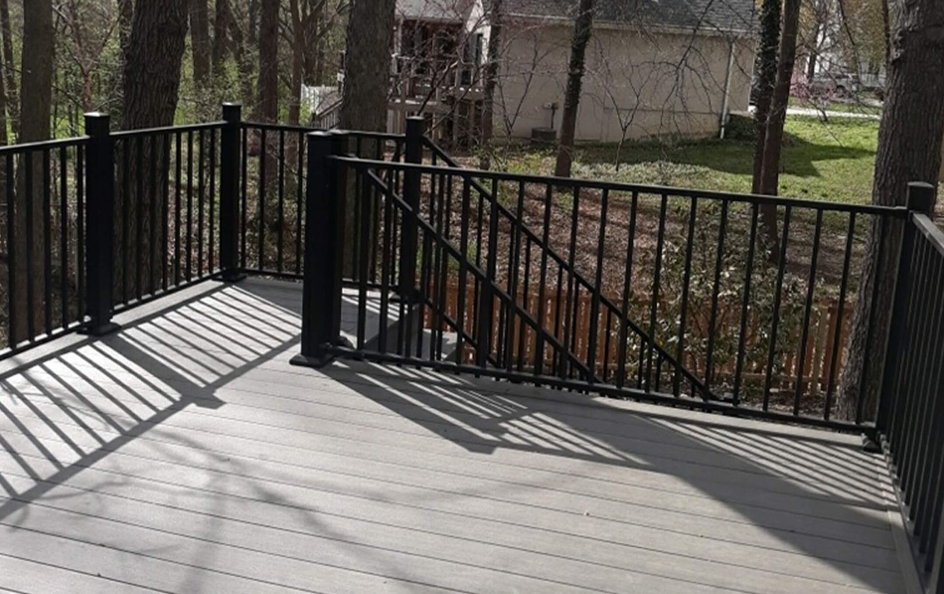 A deck with a black railing and a house in the background