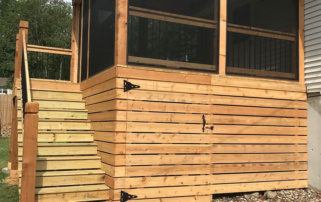 A wooden screened in porch with stairs leading up to it.