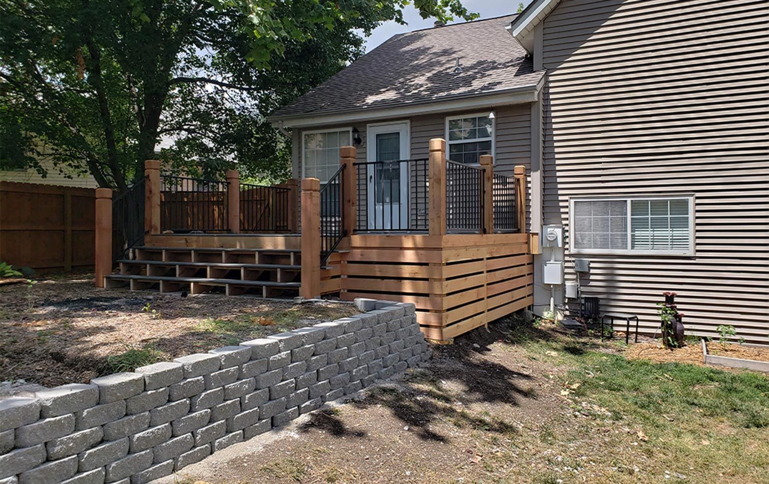 A house with a wooden deck and a brick wall in front of it.
