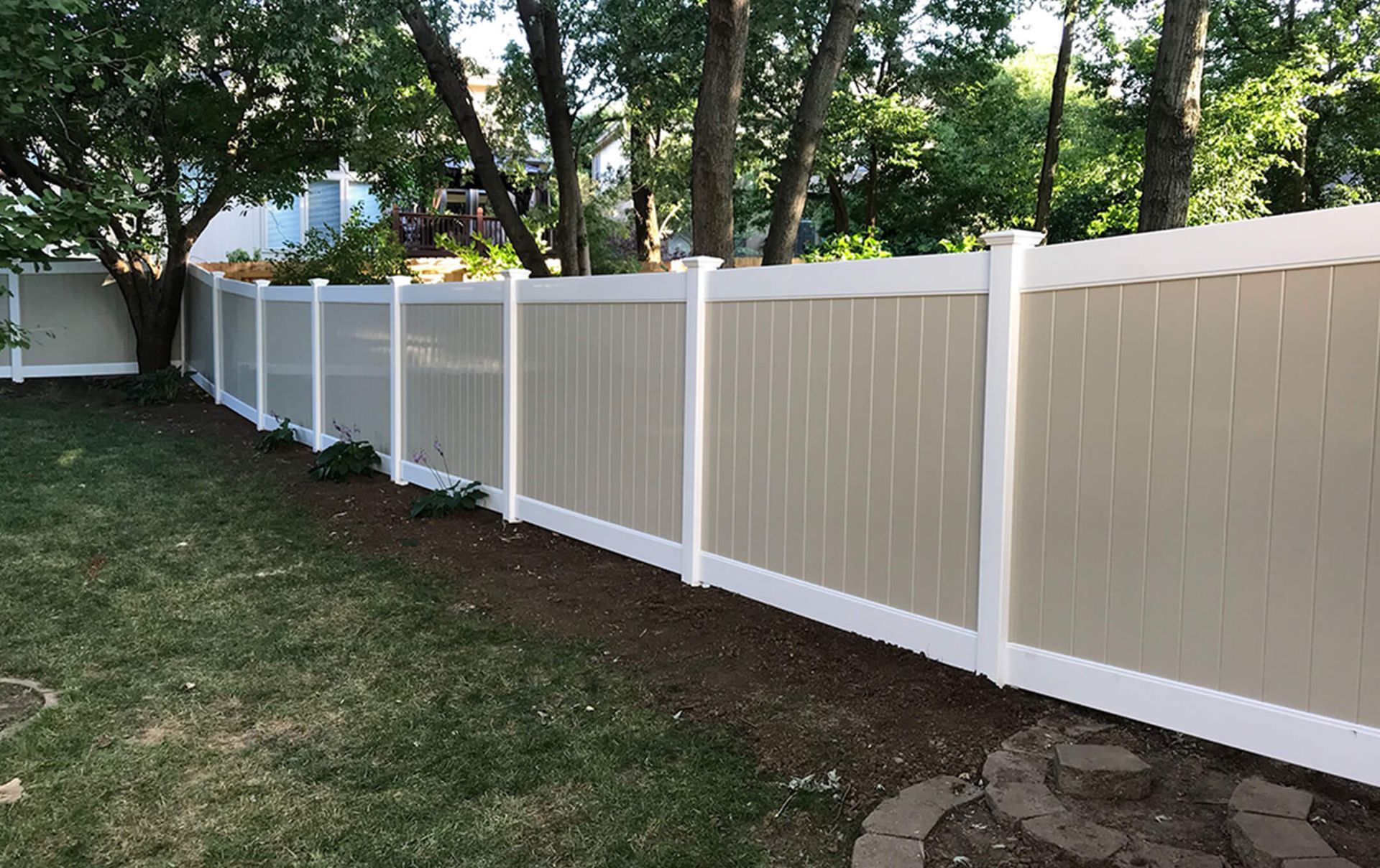 A tan and white fence surrounds a lush green yard.