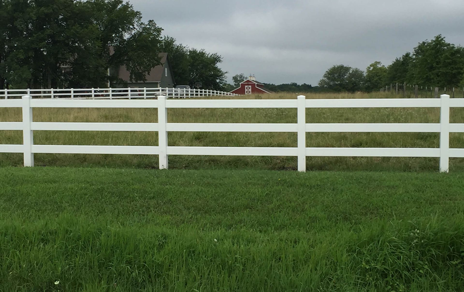 A white fence surrounds a grassy field with a red barn in the background.