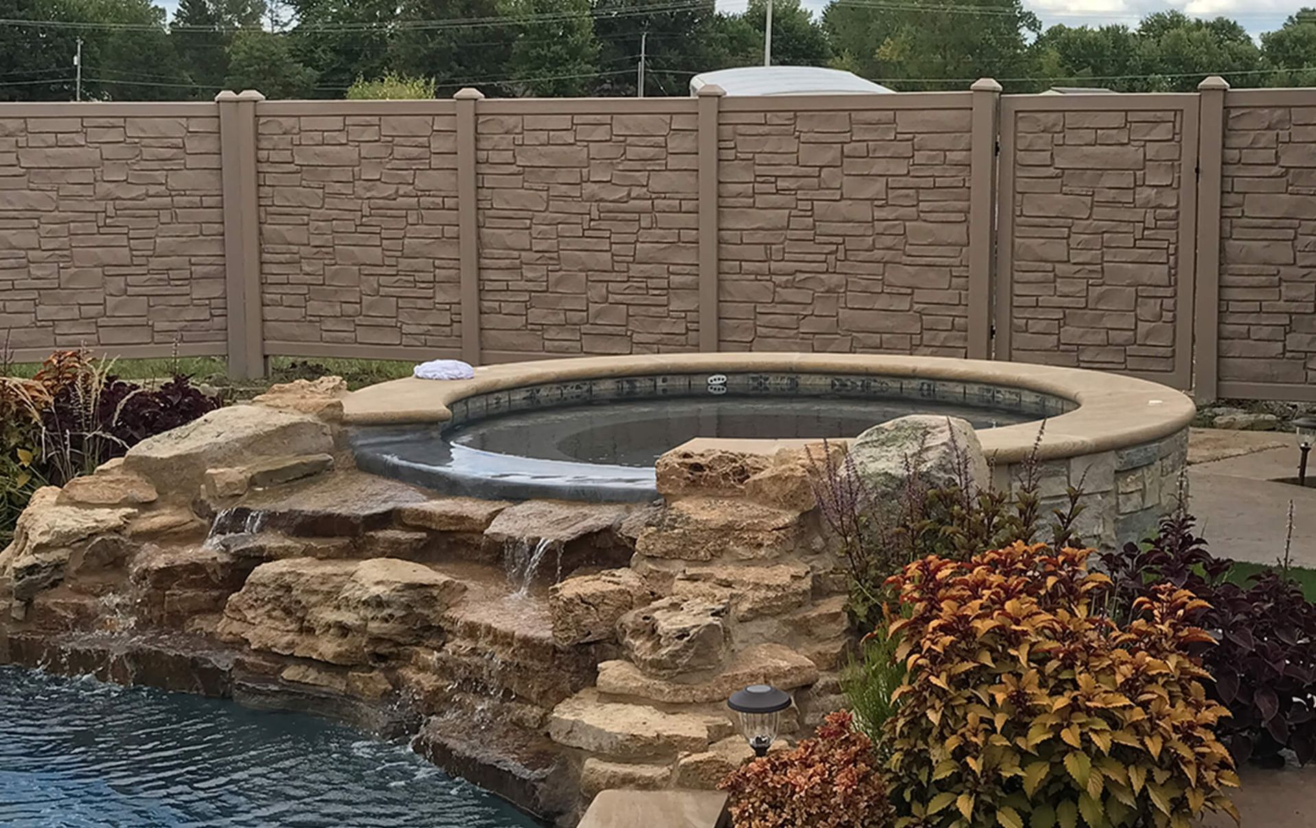 A swimming pool with a hot tub and a waterfall in the backyard.
