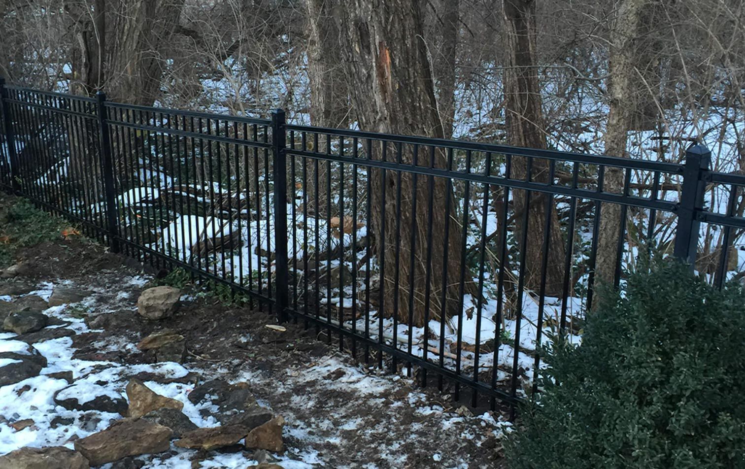 A black metal fence is in the middle of a snowy forest.