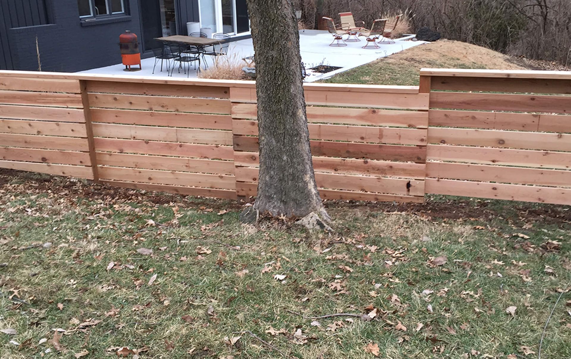 A wooden fence is surrounding a tree in a backyard.