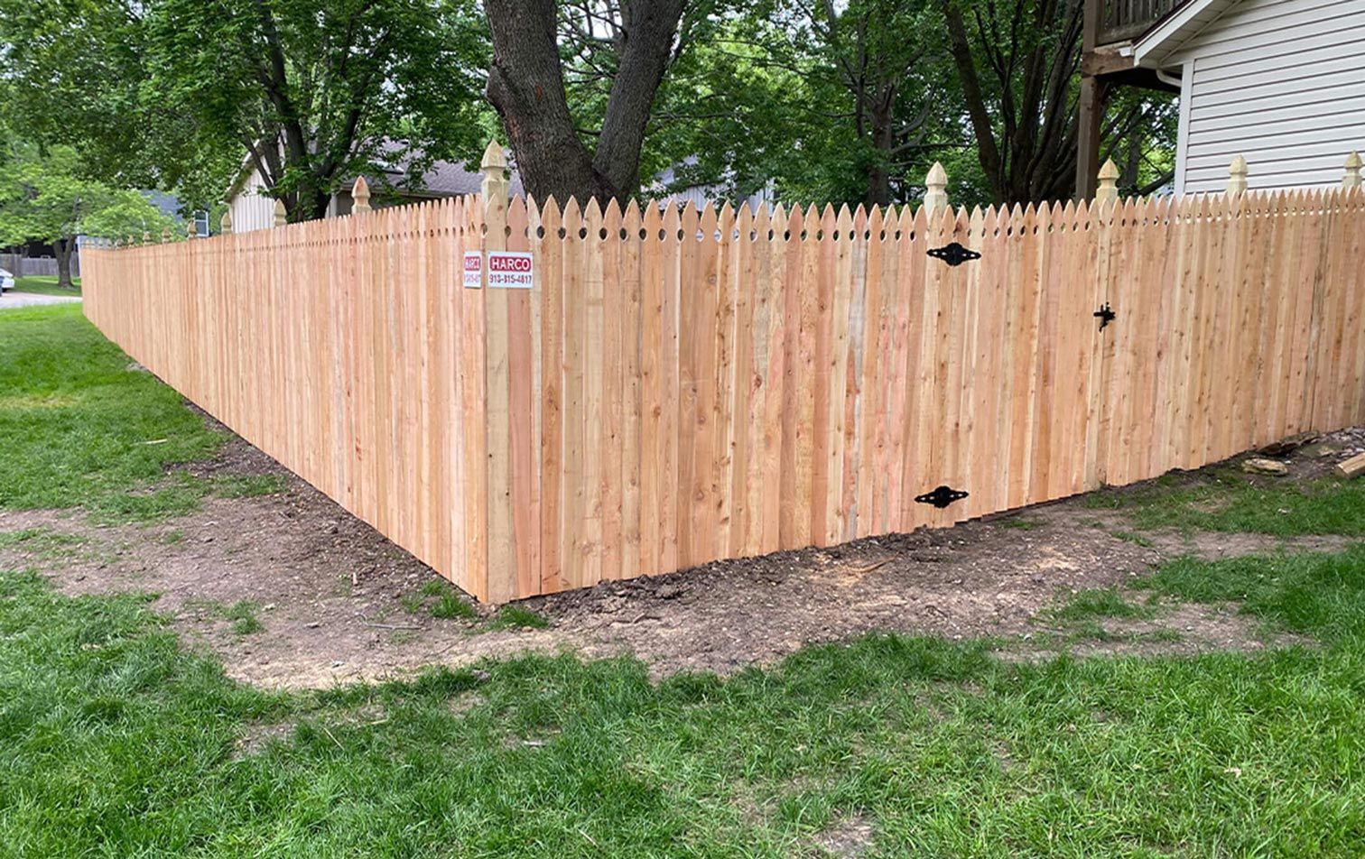 A wooden fence is sitting in the middle of a lush green yard next to a house.