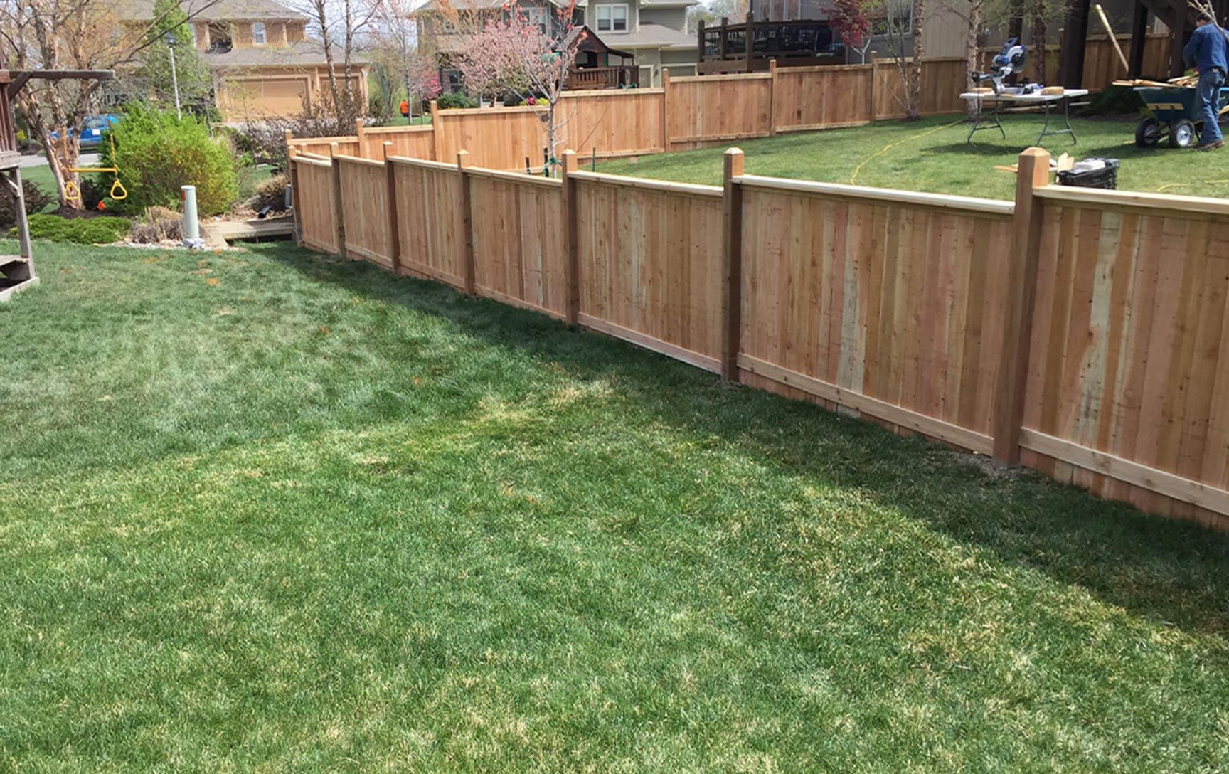 A wooden fence surrounds a lush green lawn in a backyard.