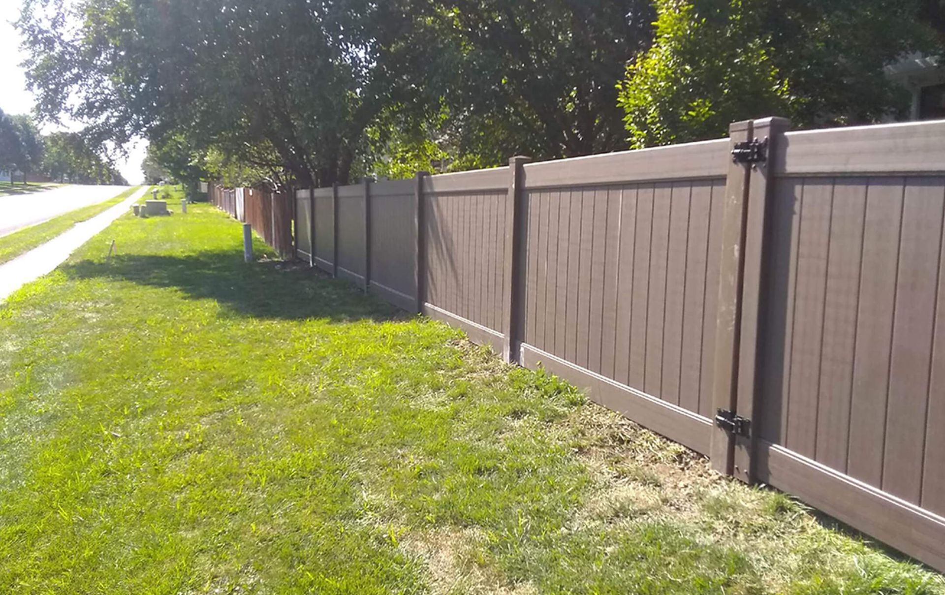 A brown fence surrounds a lush green lawn next to a sidewalk.