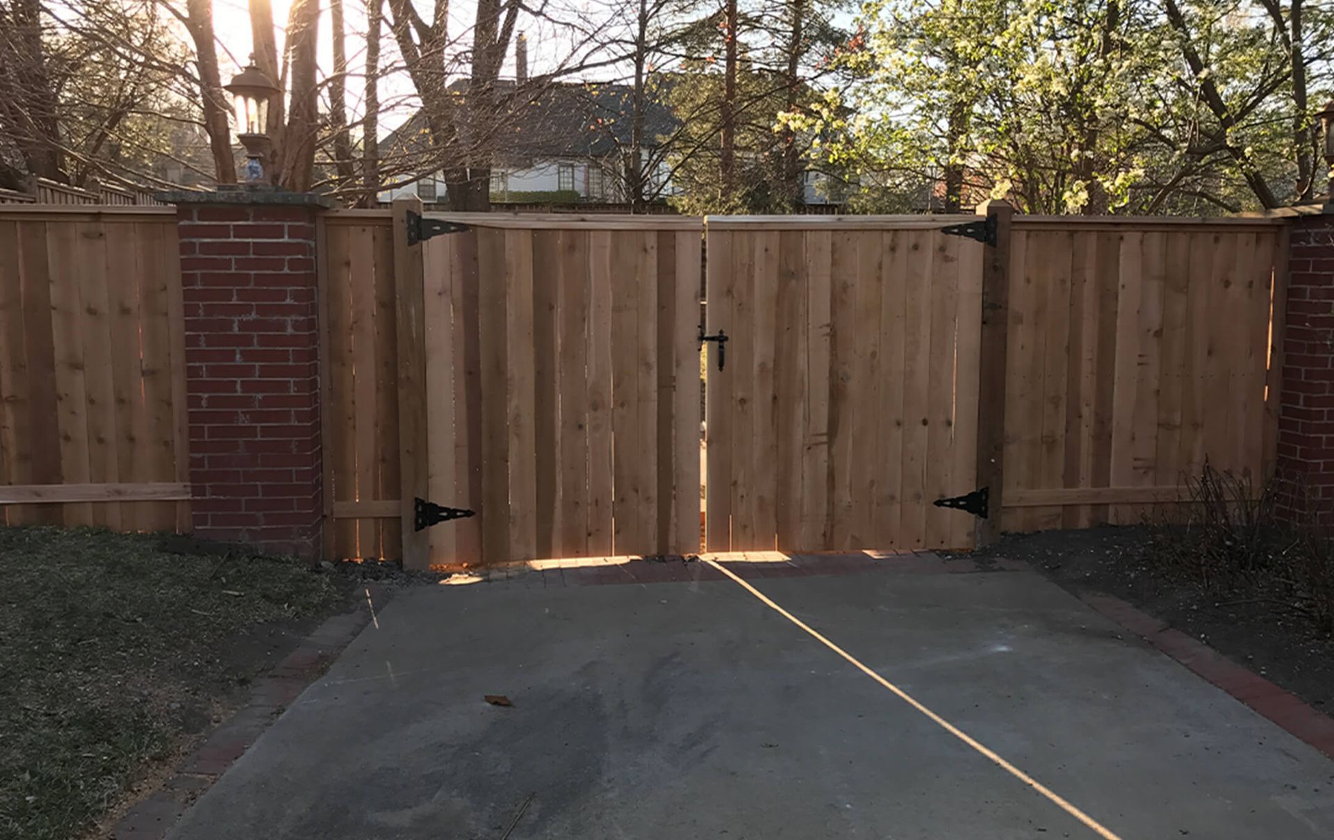 A wooden fence with a gate in the middle of a driveway.