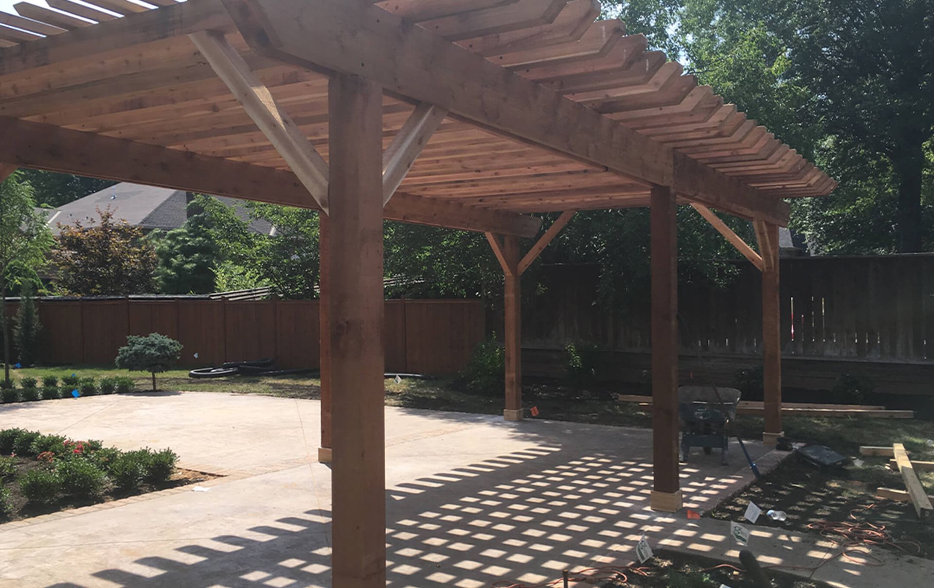A wooden pergola is sitting on top of a concrete patio in a backyard.