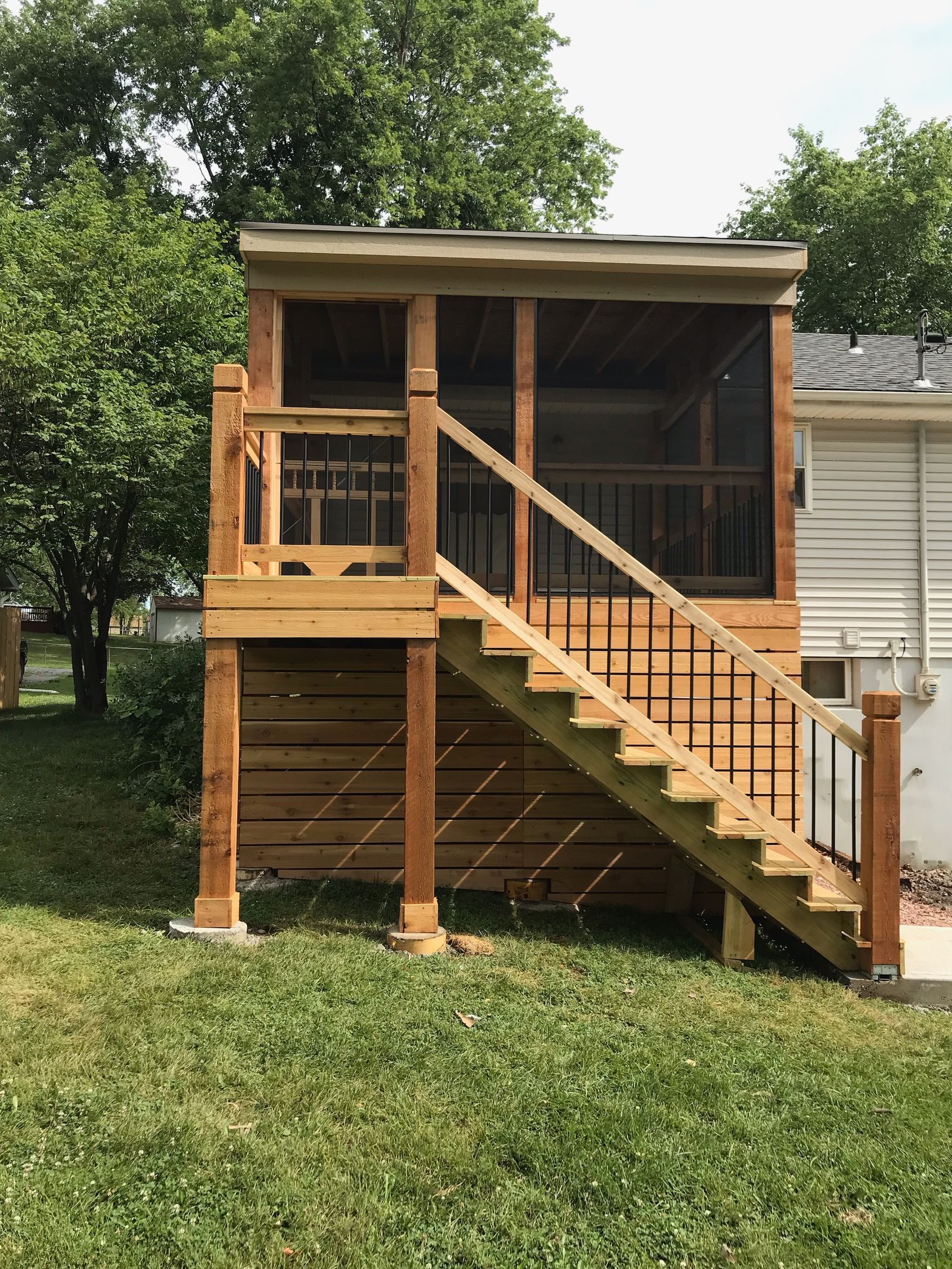 Wooden screened-in porch with stairs, railing, and a small roof, elevated above ground level.