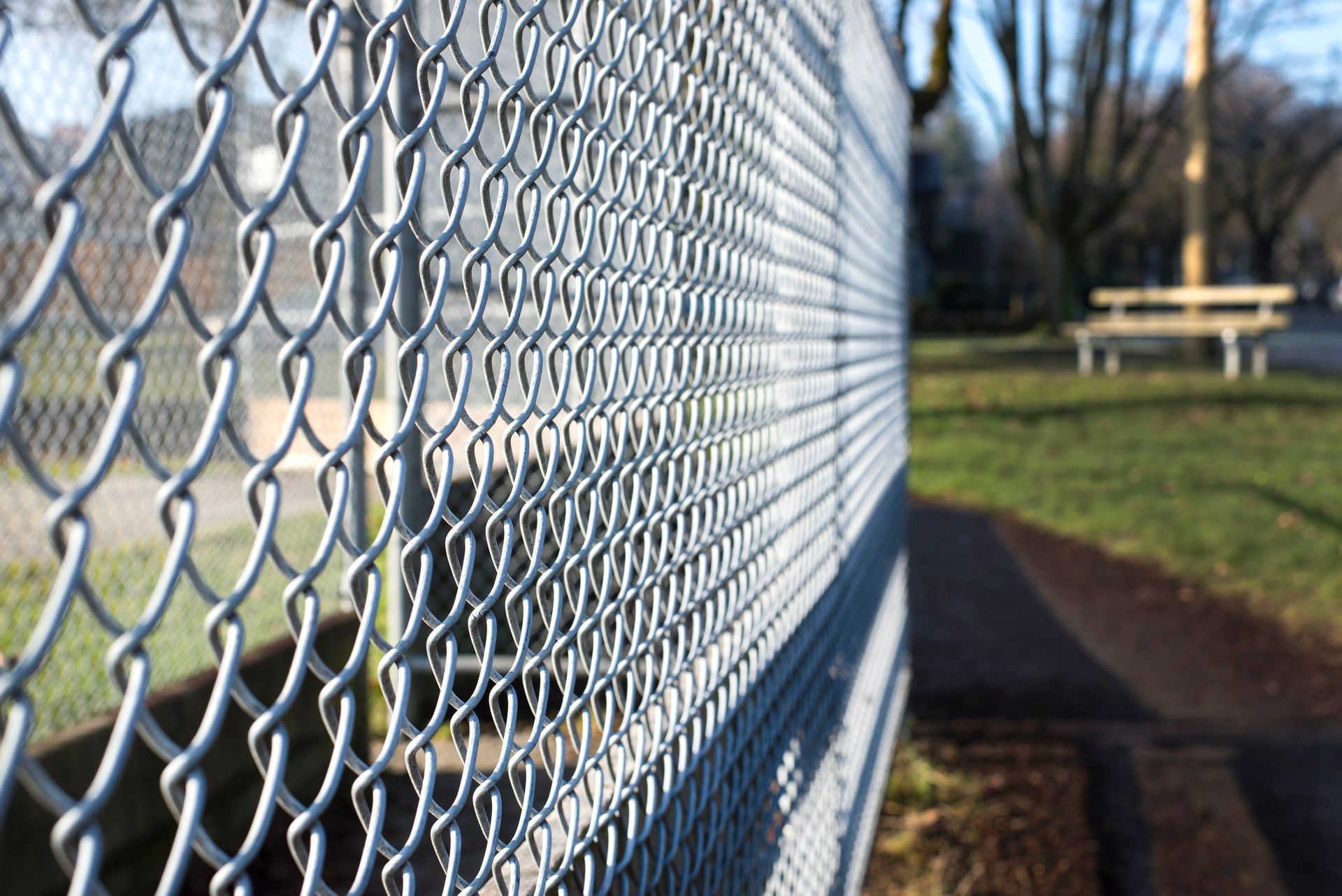 A chain link fence in a park with a picnic table in the background.