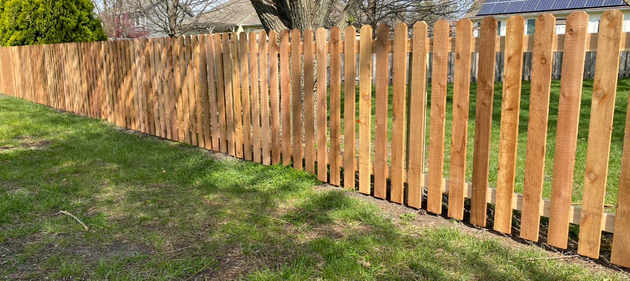 A wooden picket fence is sitting in the middle of a lush green field.
