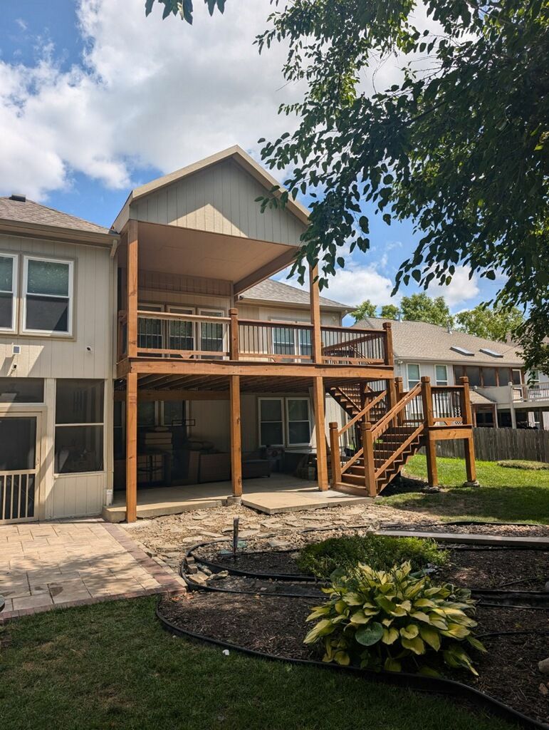 Two-story wooden deck attached to a house with a shaded upper level and stairs leading to the yard.
