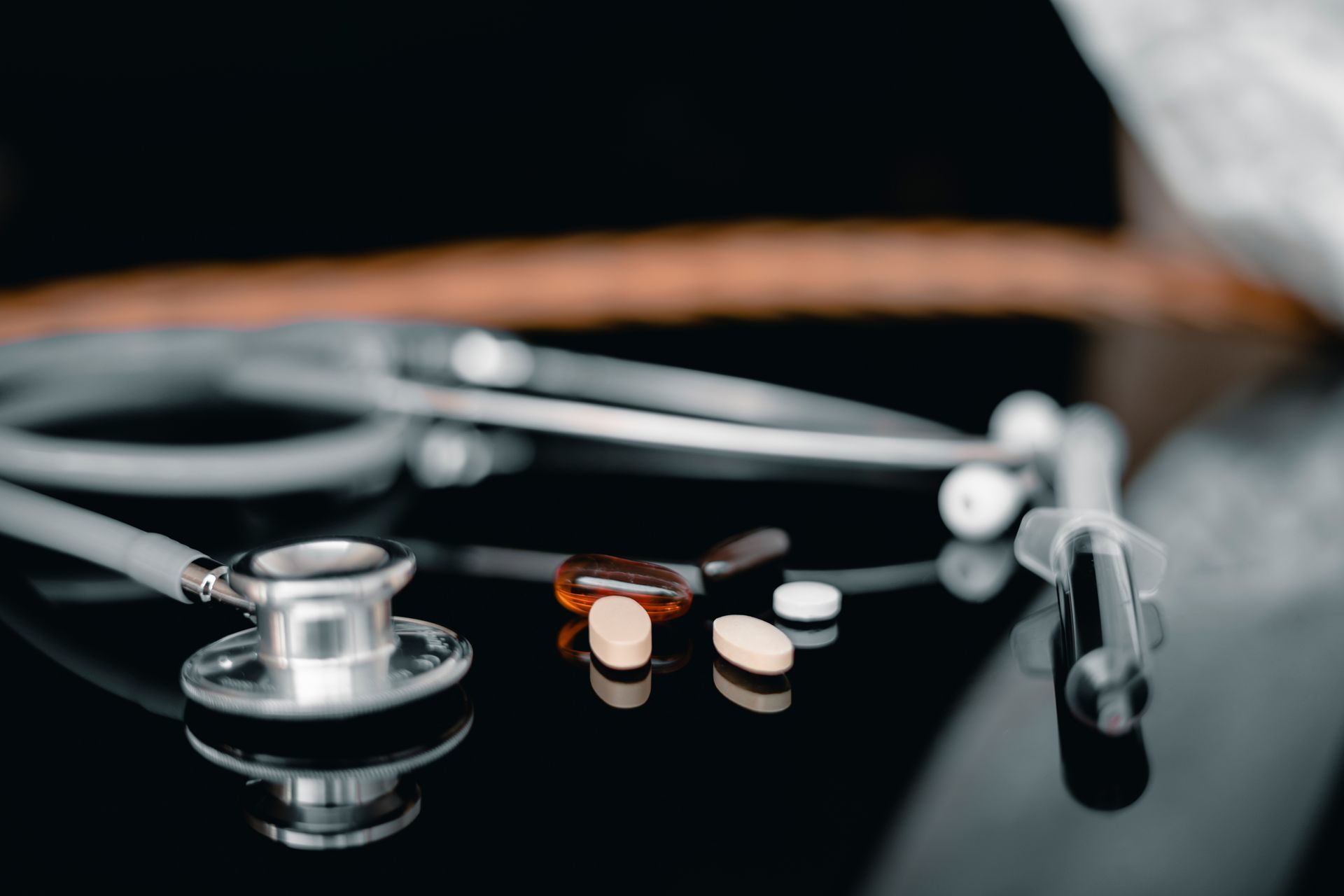 Stethoscope, pills, and syringe on a shiny black surface, suggesting medical care and treatment.