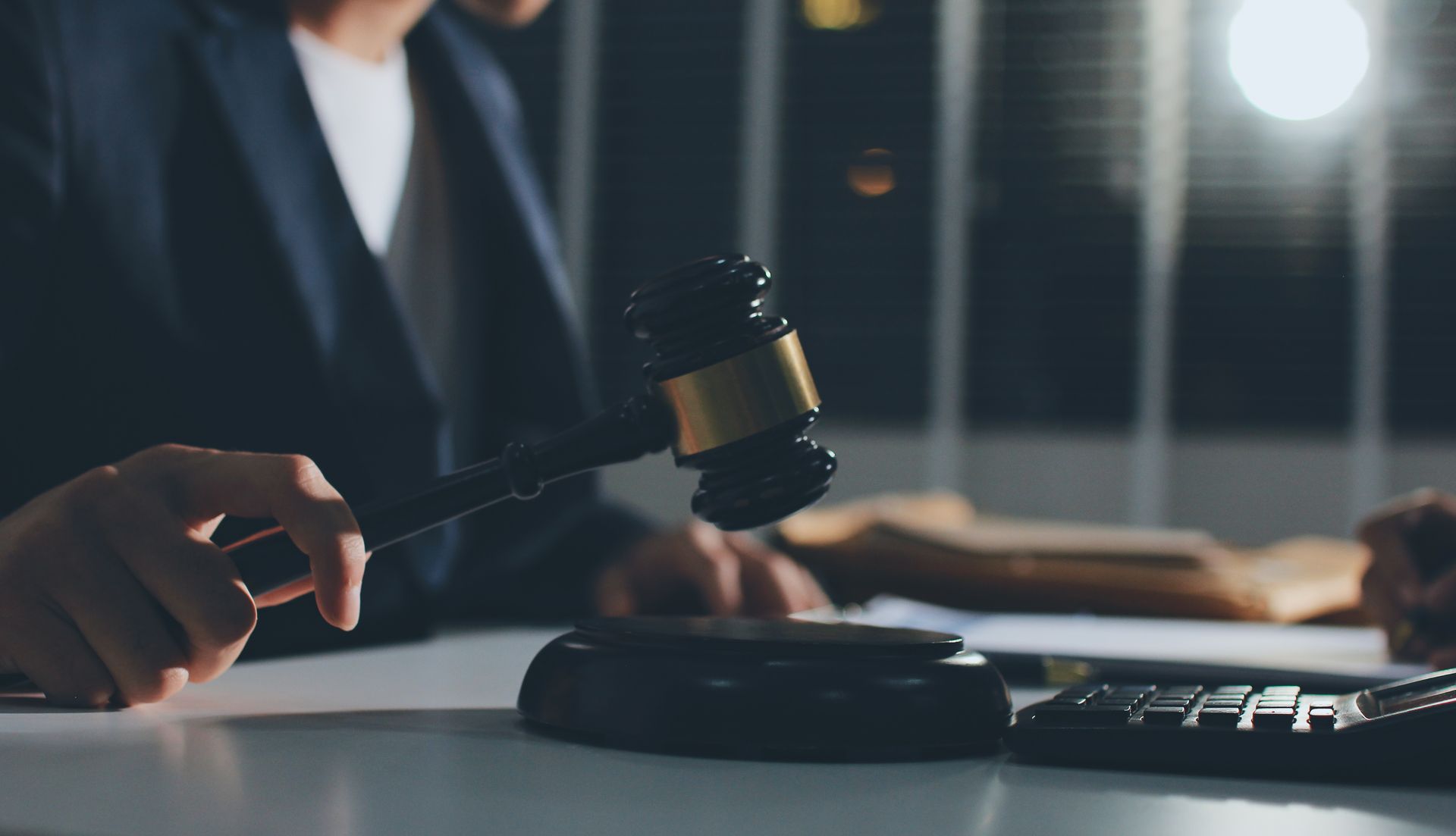 A person in a dark suit holding a gavel, striking a wooden block on a desk.
