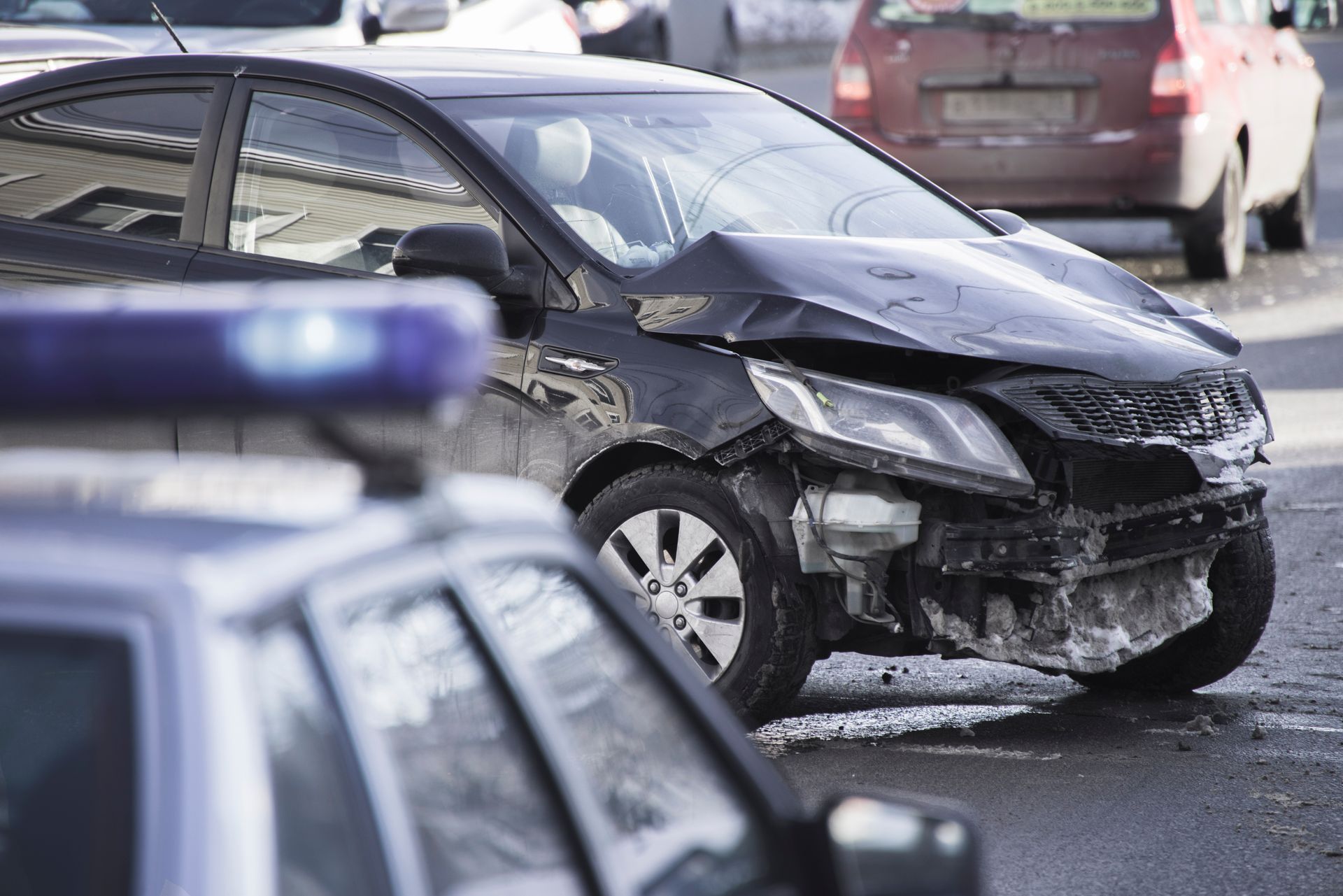 Car accident scene with damaged black car in front of a police car.