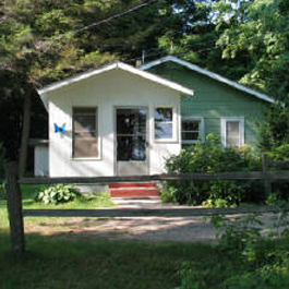 A small green and white house with a wooden fence in front of it