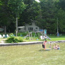 A group of children are playing in a lake with a house in the background