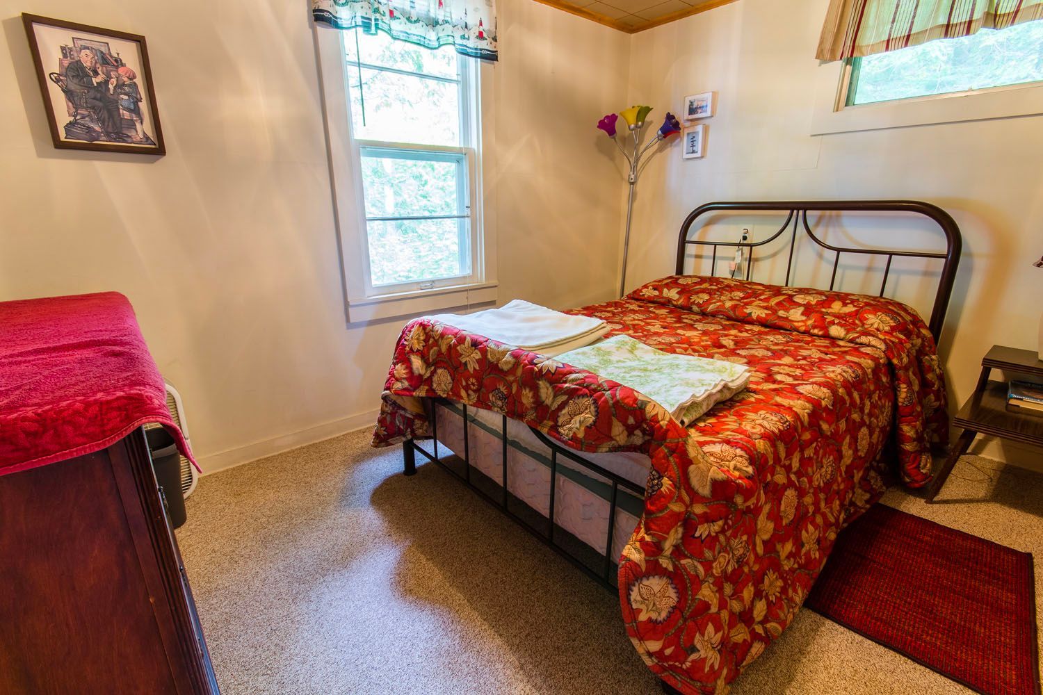 A bedroom with a bed , dresser , lamp and window