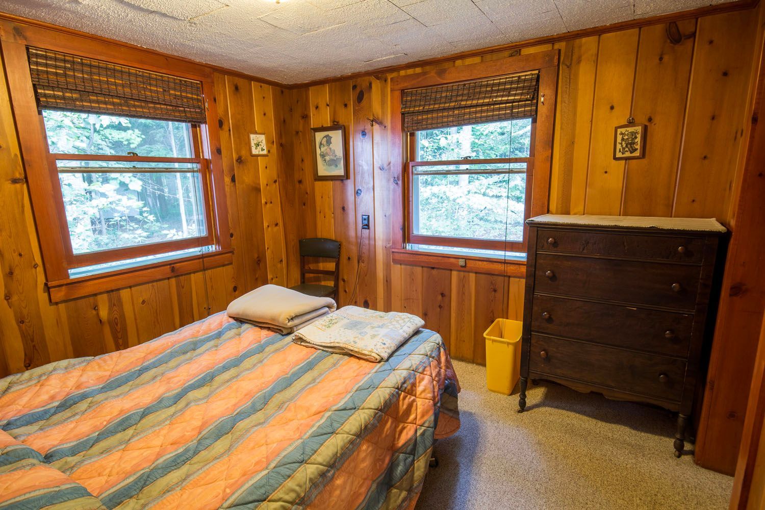 A bedroom with a bed , dresser , and two windows
