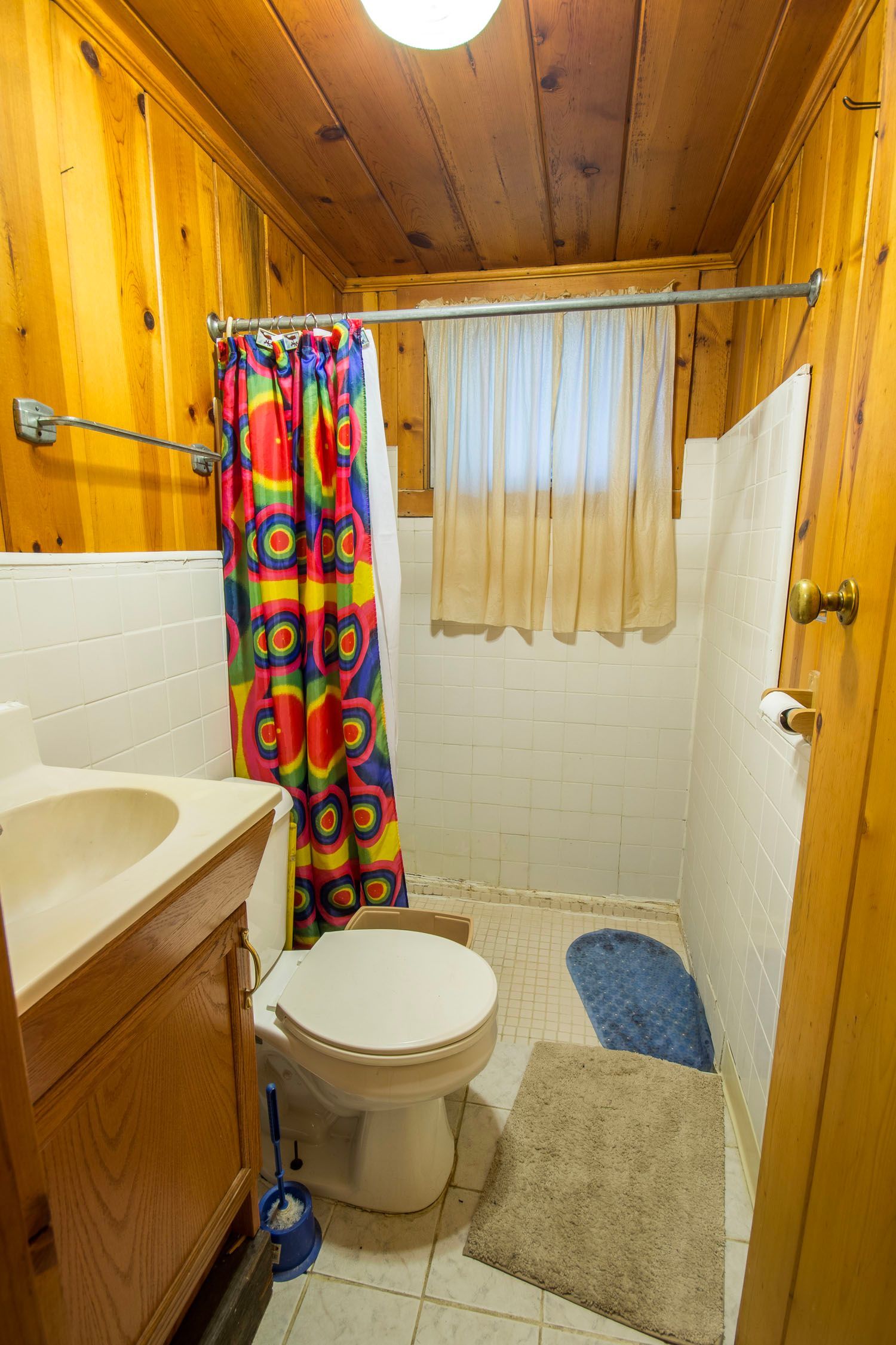A bathroom with a toilet , sink , shower and colorful shower curtain