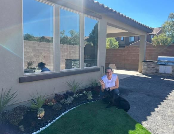 A woman is sitting on the grass with a dog in front of a house.