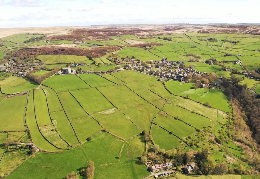 Green fields with stone walls, village in the distance under a bright sky.