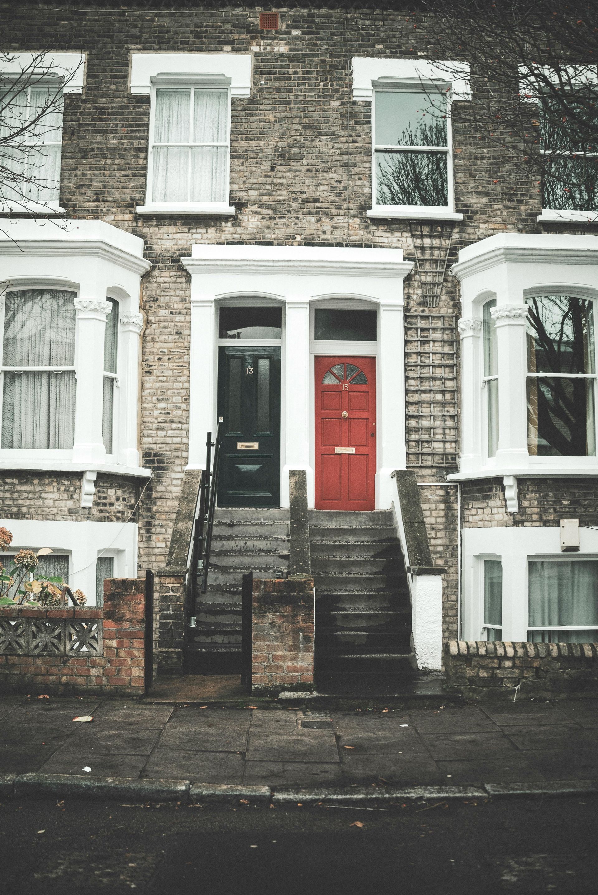 Row of brick townhouses with a black and red front door, and bay windows.