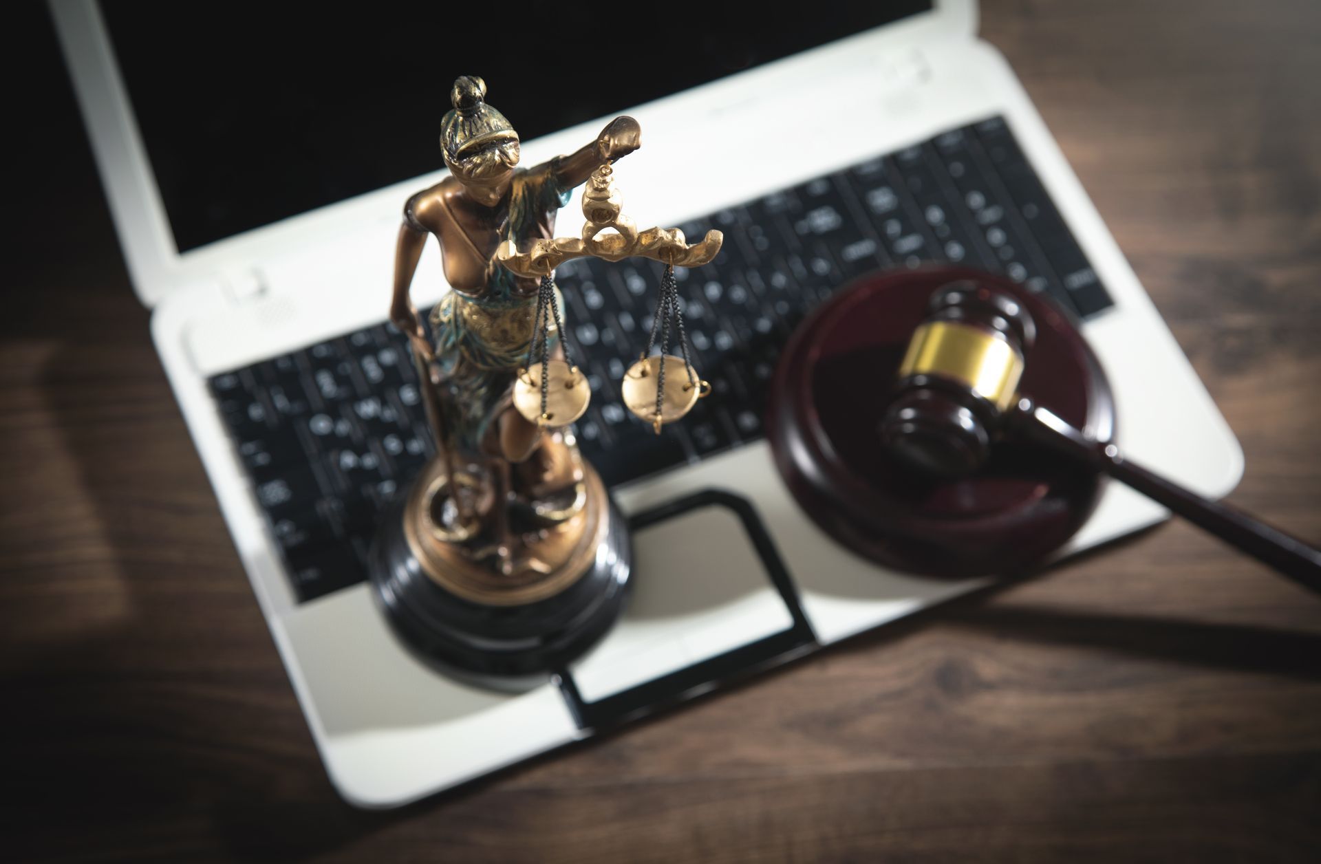 Una statua della giustizia è appoggiata su un computer portatile, accanto a un martelletto.
