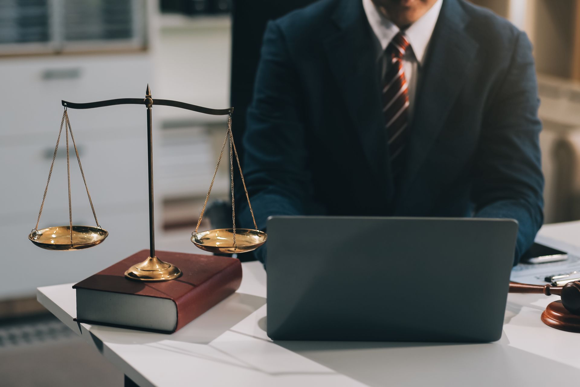 Un uomo in giacca e cravatta è seduto a una scrivania con un computer portatile e una bilancia della giustizia.