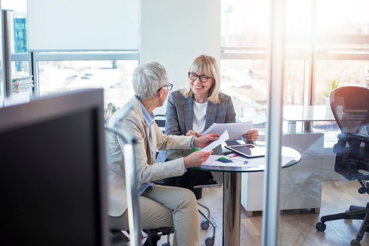 A man and a woman are sitting at a table looking at papers. A man and a woman are sitting at a table looking at papers.