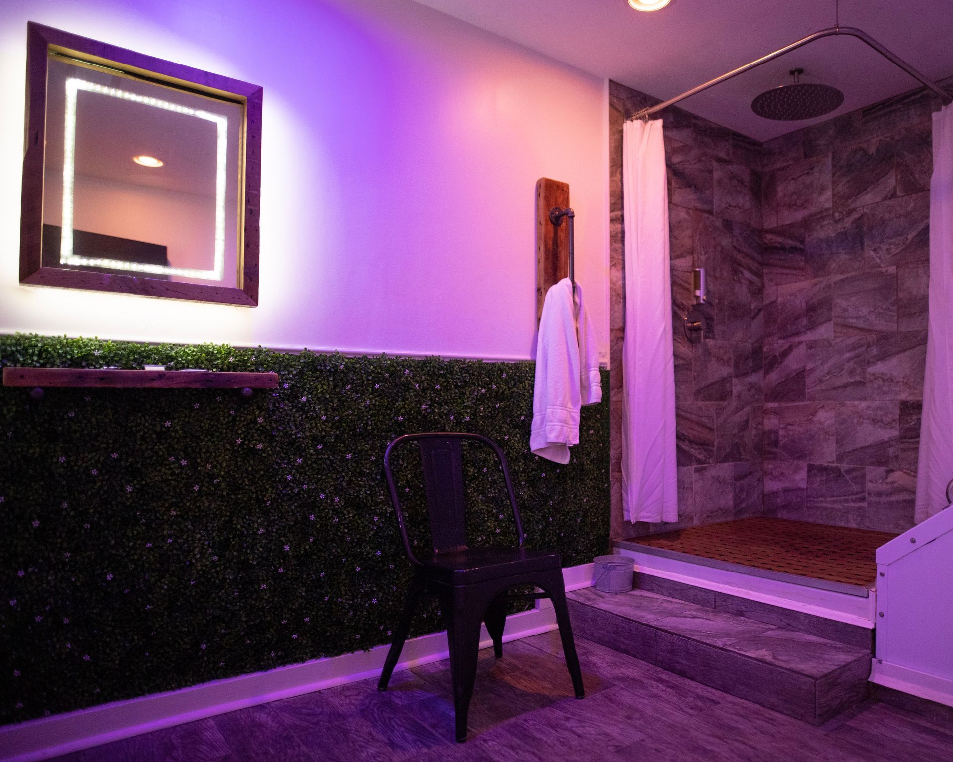 A bathroom with a chair , mirror , and shower.
