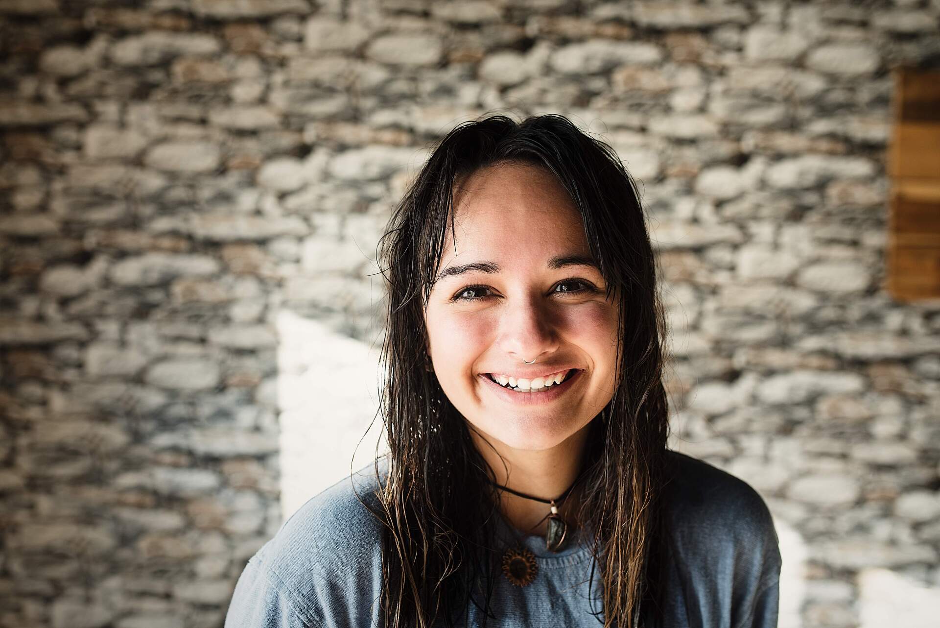 A woman with wet hair is smiling in front of a stone wall.