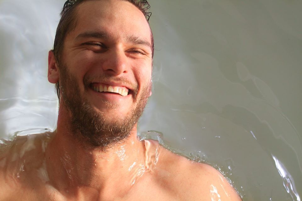 A shirtless man is taking a bath and smiling.