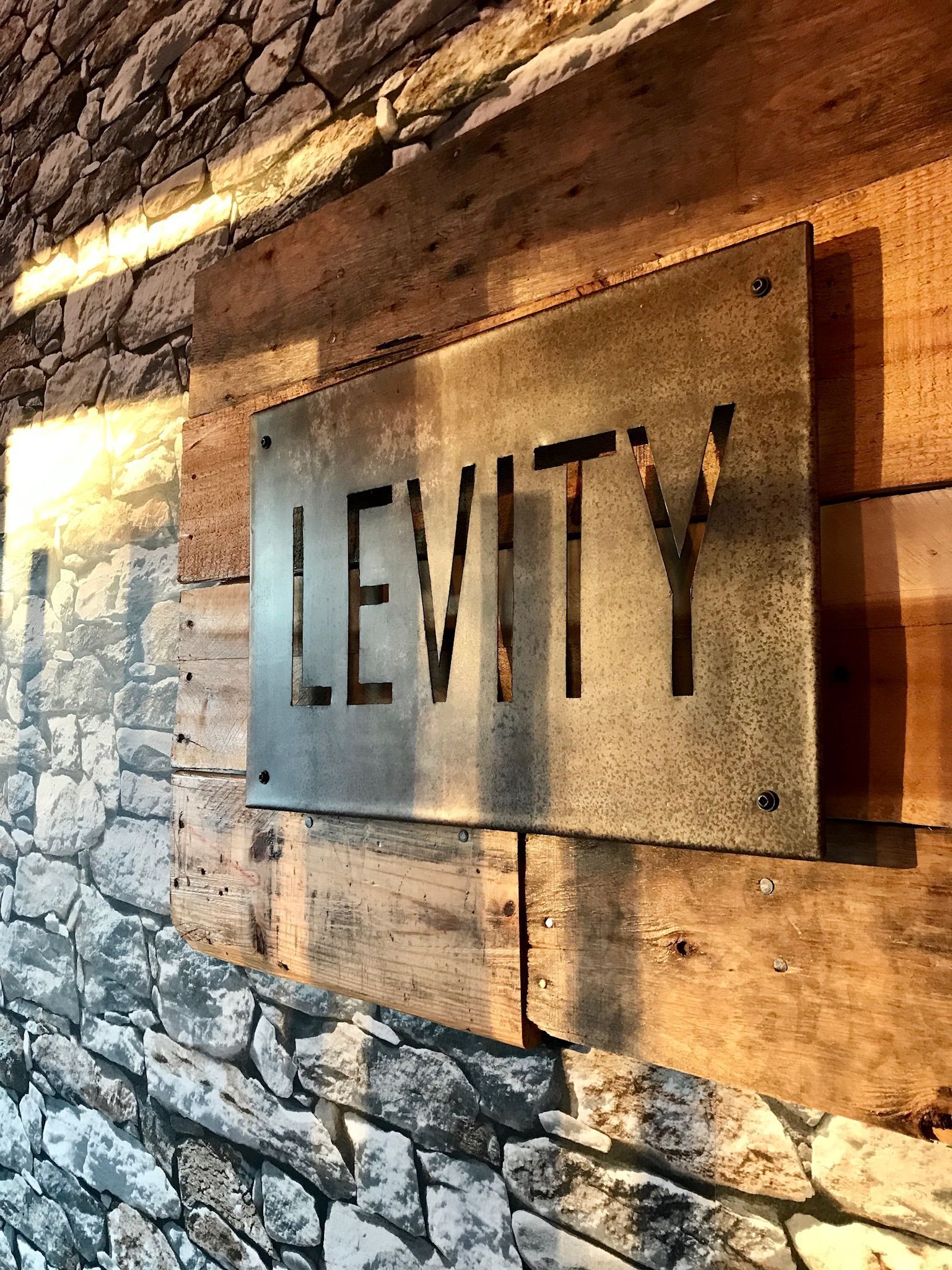 A metal sign on a wooden wall that says levity.