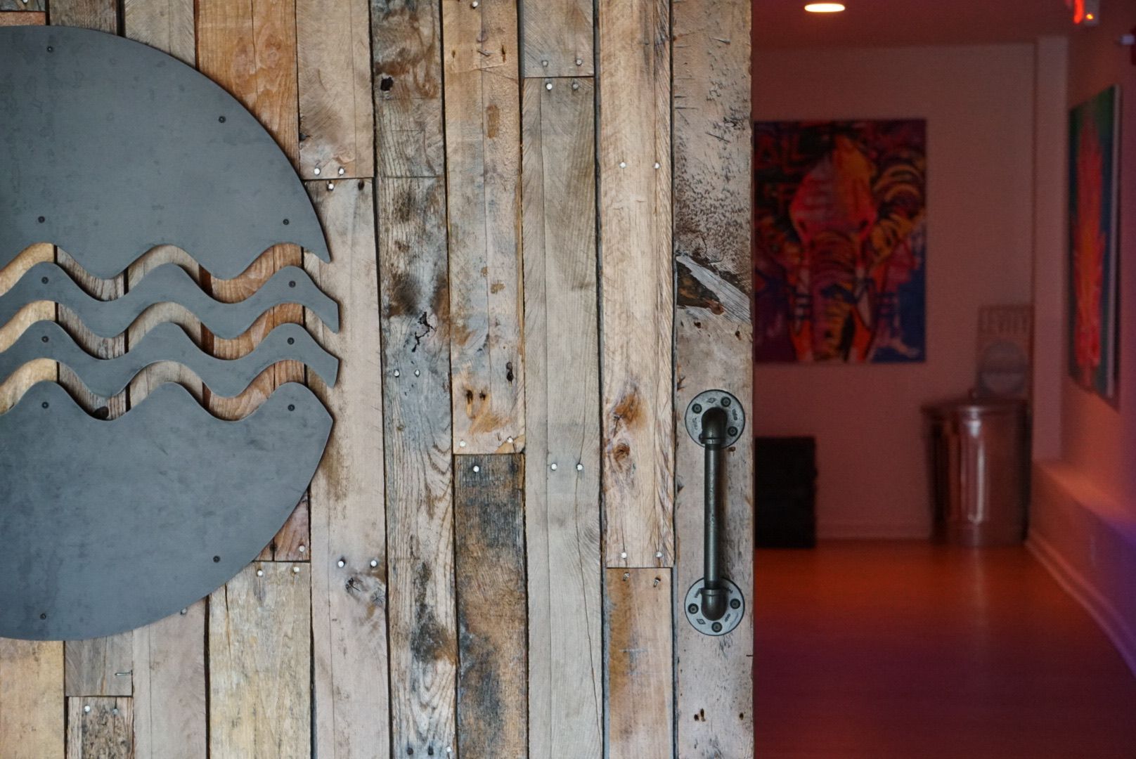 A wooden door with a metal sign on it is open to a room with a painting on the wall.