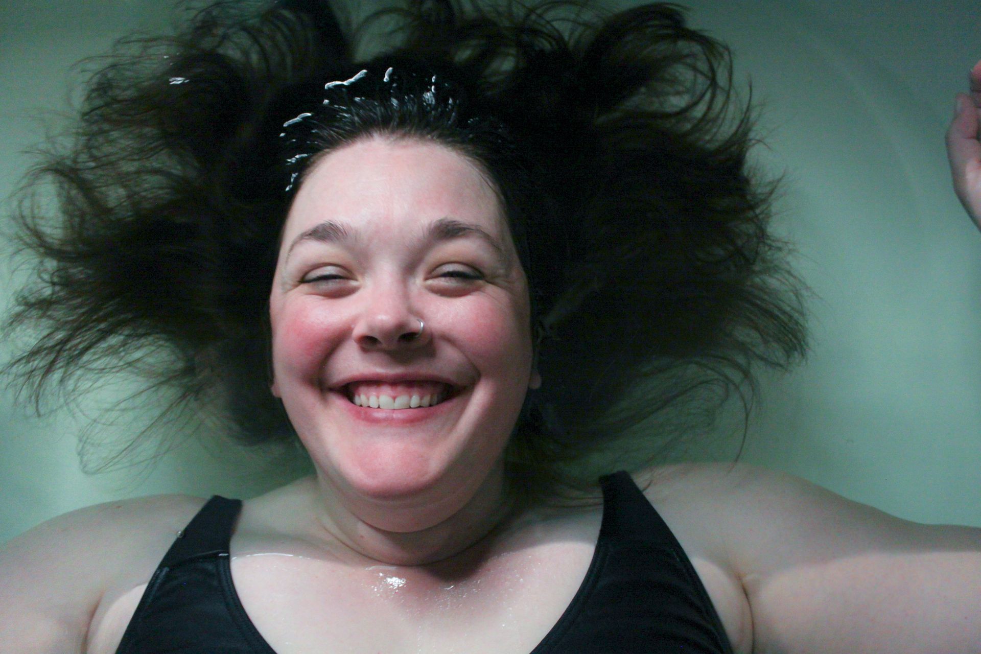 A woman in a black tank top is smiling with her hair blowing in the wind