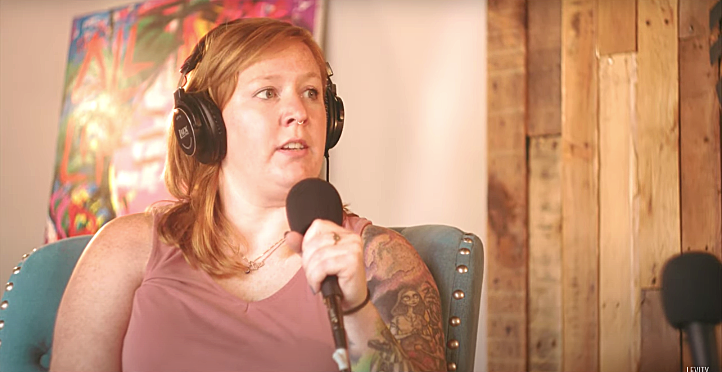 A woman wearing headphones is sitting in a chair holding a microphone.