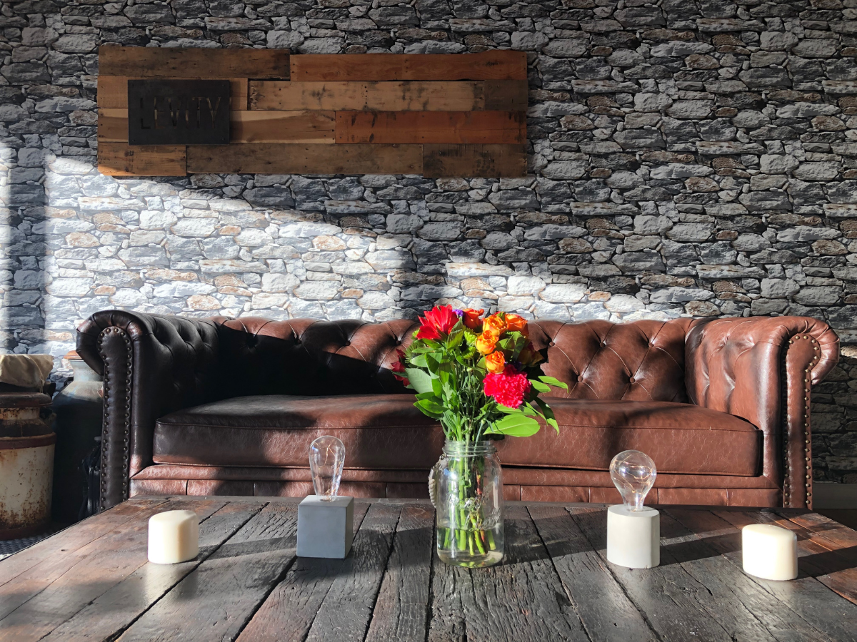 A living room with a brown couch and a vase of flowers on a wooden table.