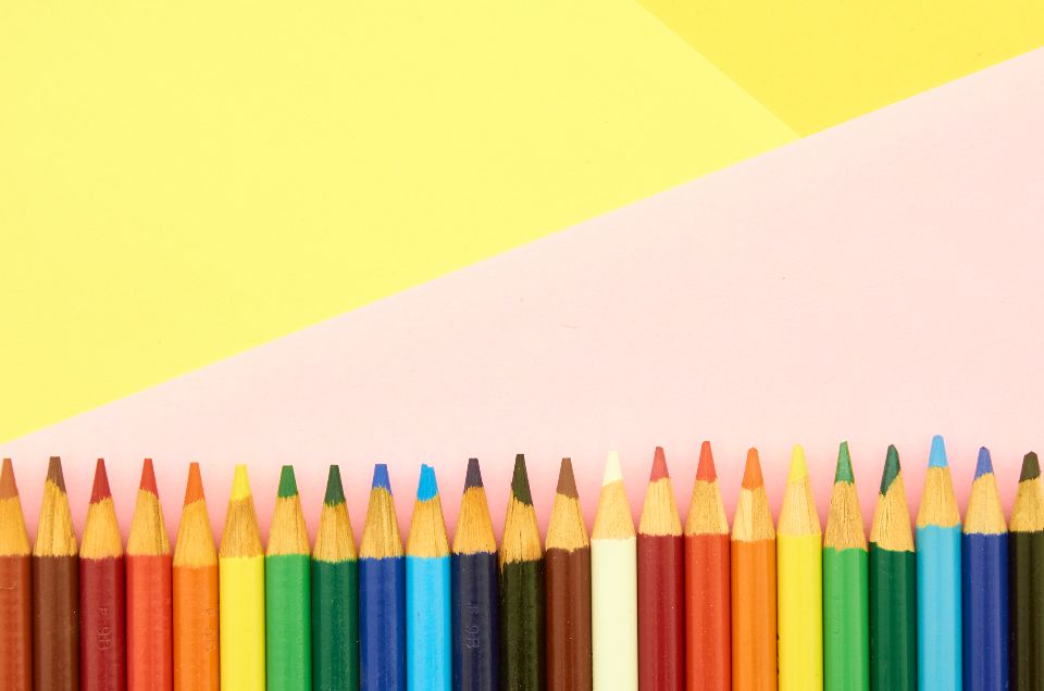 A row of colorful pencils on a pink and yellow background.